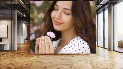 Spring girl face. Close up portrait of tender woman at sakura flowers background. Hanami celebration in sakura blooming garden. Young stylish woman standing in sakura park and enjoy beauty of pink Wall mural