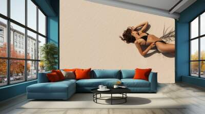 Top aerial drone view of woman in swimsuit relaxing and sunbathing on beach Near The Ocean. Attractive brunette girl in black bikini laying on a sandy coast with palm leaf. Gorgeous tanned mixed race Wall mural