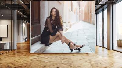 Travel tourist girl on vacation posing on city street. Attractive young romantic passion woman sitting on sidewalk against beautiful view on venetian quiet street in Venice, Italy. Gorgeous mixed race Wall mural