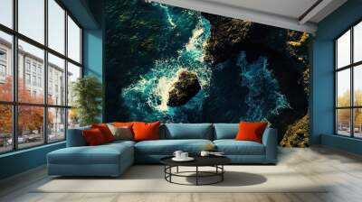 Aerial view of rocky coastline with vibrant blue waves crashing against the shore during sunny daylight hours Wall mural