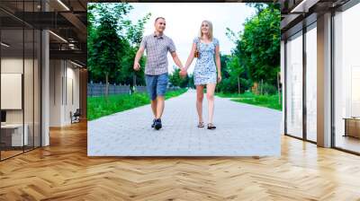 The guy with girl in a summer park holding hands walking relax, enjoy stroll, happy family concept slogan your text in background. City life. lot of greens. Wall mural