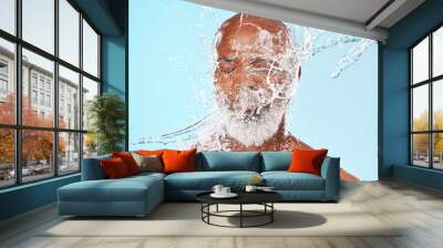 Elderly black man, water splash and face in studio for wellness, clean or facial health by backdrop. Man, model face and water for skincare, healthy self care or cosmetic beauty by blue background Wall mural