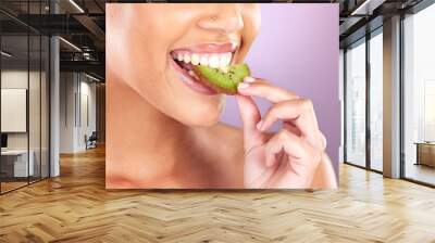 Woman, face and kiwi for skincare beauty wellness, natural cosmetic health and fruit nutrition diet in purple studio background. Model eating, vitamin c and facial smile for organic skin or body glow Wall mural