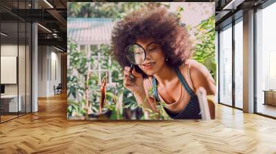 Woman, gardening and farmer with magnifying glass for carbon capture, plants or flower growth in outdoor garden. Black woman, nature and earth day or natural agriculture sustainability greenhouse Wall mural