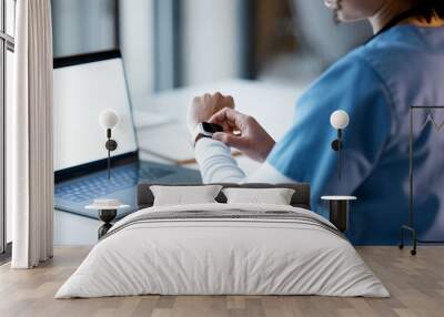 Smartwatch, healthcare and time with a woman nurse working late at night on a laptop in the hospital. Medical, watch and overtime with a female medicine professional at work on a computer in a clinic Wall mural