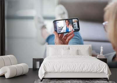 The most comfiest consultation ever. Shot of a senior woman using a smartphone to make a video call with her doctor on the sofa a home. Wall mural