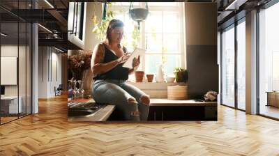 Trendy woman browsing internet on tablet using her new wifi at home looking happy and satisfied. Normal, real and edgy young female searching online for cool recipe ideas to use in her modern kitchen Wall mural