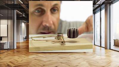 Close up shot of a man looking eagerly at eating a sweet chocolate that is in a mouse or rat trap which indicates that he should not eat it or is on a diet. Wall mural