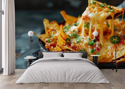 Chip pulled out of bowl of cheese covered nachos on dark background, food photography concept Wall mural