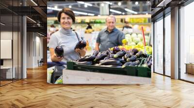 Elderly buyer woman chooses ripe eggplant on grocery store window Wall mural