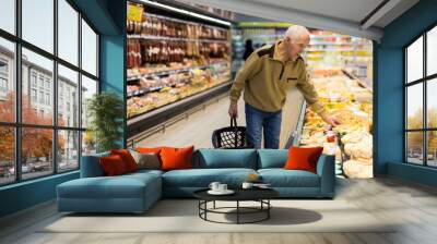 elderly man choosing cheese in supermarket Wall mural