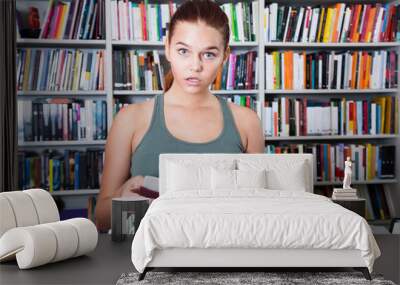 girl surprised chooses a book in the library Wall mural