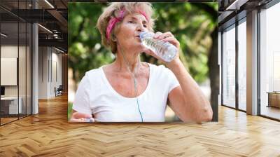 Mature sportswoman drinking water in park Wall mural