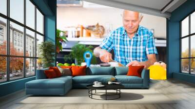 senor man preparing fresh vegetable salad at home in the kitchen Wall mural