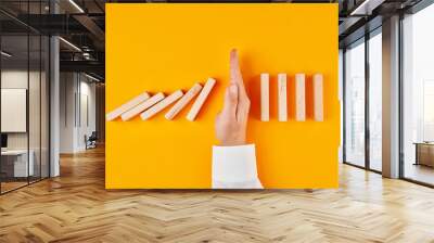 Hand of a businessman stopping domino effect on yellow background Wall mural