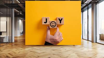 Hand places the word joy on wooden blocks with a smiling face symbol. Joy, happiness, pleasure, joyful emotion. Wall mural