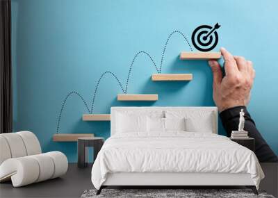 Male hand arranges a wooden block staircase with target icon. Achieving goals and objectives or goal setting Wall mural