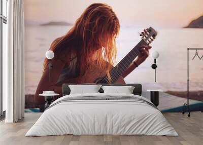 Silhouette of a blonde female playing acoustic guitar on the beach at sunset Wall mural