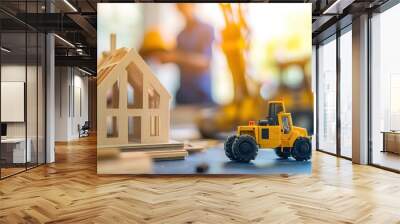 Model of a house and construction equipment on a table, with two people working facing each other behind it, blurred background Wall mural