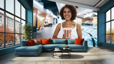 Curly-haired woman with an afro hairstyle in a white shirt is walking to watch a movie with popcorn in hand Wall mural