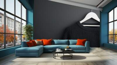 A stylish black sweater hangs on a white hanger against a sleek dark background, showcasing modern fashion aesthetics. Wall mural