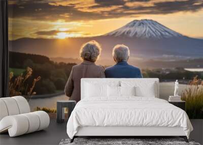 A mature older couple with grey hair sitting outdoors watching the sunset over a lake with a mountain in the background.  Wall mural