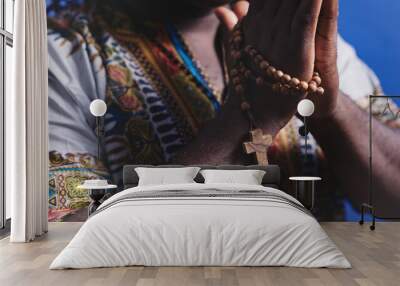 Unrecognizable African black man in traditional dress with rosary praying with hands over his chests. High quality photo Wall mural