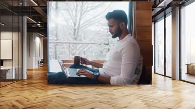 Young man relaxing near the window with coffee and browsing social media. High quality photo Wall mural