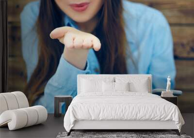 Cropped image of beautiful young girl with smart phone in hands shows air kiss gesture sitting on the background of wall of wooden boards. Photo with depth of field. Wall mural