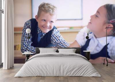 Little elementary school student boy tries to disturb the girl during the lesson. Boy tries to reach the girl's back. Conflict. Wall mural