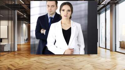 Young beautiful businesswoman is standing in an office with a male colleague at the background. Concept of success in a business Wall mural