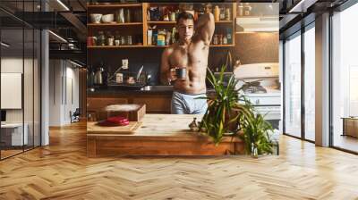 Enjoying a cup of coffee in the kitchen. Cropped shot of a handsome young shirtless man drinking a cup of coffee in the kitchen at home. Wall mural