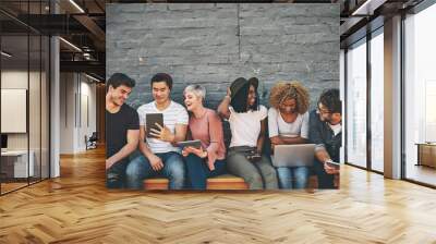 Group of friends on digital devices and social media sitting together while smiling and talking. Technology obsessed online remote workers taking a break. Happy casual creative team outside Wall mural