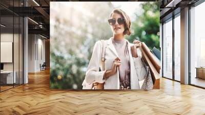 Trendy, fashionable and elegant woman enjoying shopping in the city. Young female coming from a sale downtown, holding shopping bags while looking satisfied. Lady spending the day on retail therapy Wall mural