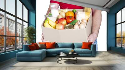 Grocery delivery courier man in red uniform holds cardboard box with fresh vegetables, fruits and other food isolated on white background. Express food delivery, donation concept. Wall mural