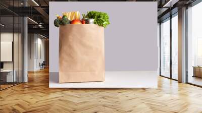 Various grocery items in paper bag on white table opposite gray wall. Bag of food with fresh vegetables, fruits, pasta and canned goods. Food delivery, shopping or donation concept. Copy space. Wall mural