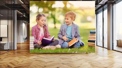 Boy and girl sitting on the meadow with books in their hands. Wall mural