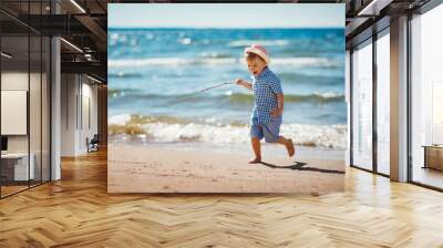 Boy walking at sea in straw hat Wall mural