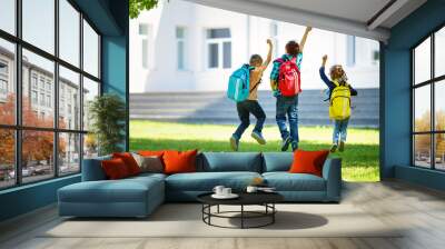 Children with rucksacks jumping in the park near school. Pupils with books and backpacks outdoors Wall mural