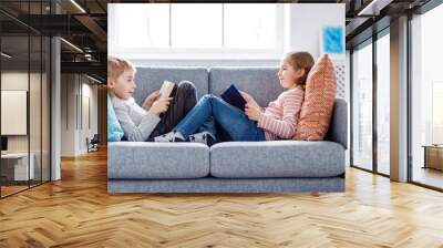 Cute children sitting on the soft sofa and reading books Wall mural