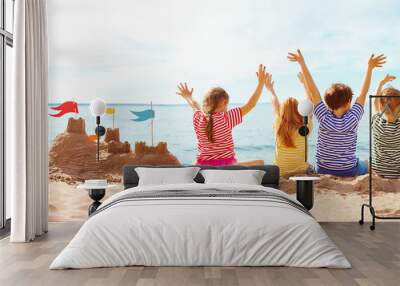 Four happy children sitting onthe sea coast and raising up their hands. Wall mural