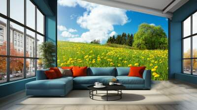 Green field with yellow dandelions and blue sky. Panoramic view to grass and flowers on the hill on sunny spring day Wall mural