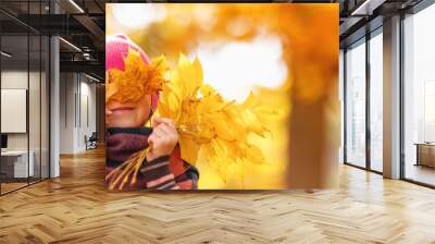 Happy child hiding his eyes behind the maple leaves. Wall mural