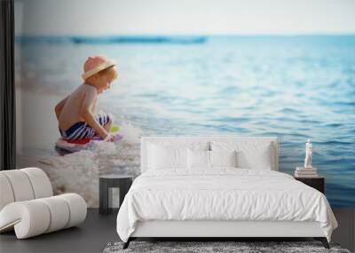 little boy walking at the beach in straw hat Wall mural