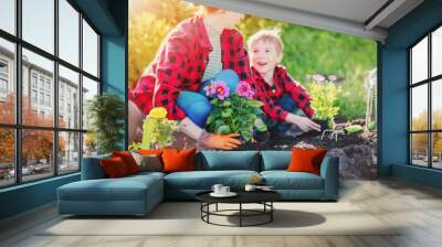 Mother with children planting sprouts in the cultivated soil. Wall mural