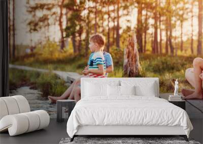 Mother with her children sitting on the pier of the swamp lake. Wall mural