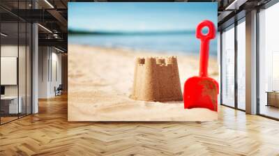 Sandcastle with a shovel on the sea in summertime. Seashore on beautiful day. Sand on the beach and blue water Wall mural