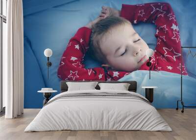 Sleepy boy lying in bed with blue beddings. Tired child in bedroom Wall mural