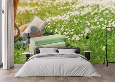 Young woman lying on the field and reading some books Wall mural