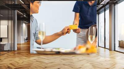 Asian couple and little kids travel ocean on summer holiday vacation. Male customer using credit card making payment after having lunch with family at beach restaurant at tropical beach in sunny day. Wall mural